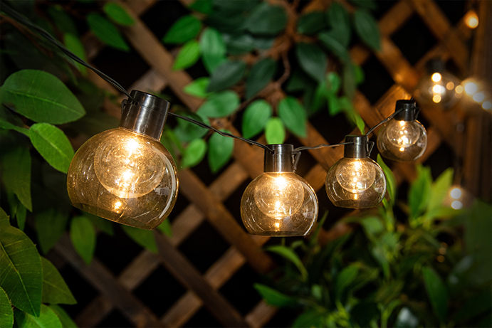 Large round solar string lights hanging on a wooden trellis fence with a warm glow