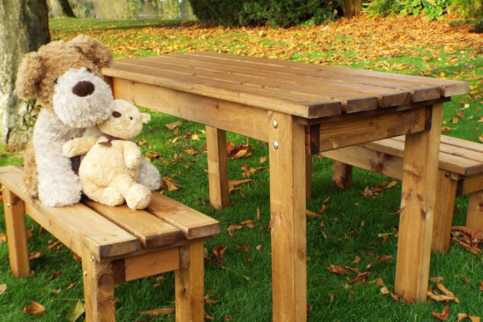 Cuddly dog toy and teddy bear sitting on a wooden benches and table set designed for children.