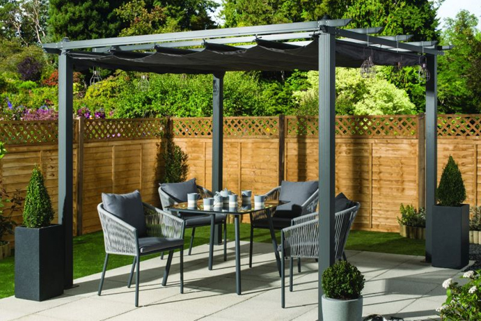 Charcoal pergola style gazebo covering a grey rattan dining set in the garden.