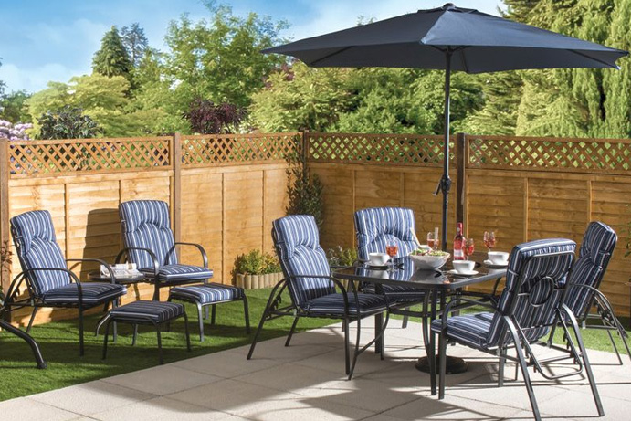 Metal garden furniture set with blue striped cushions and parasol on a patio in the sunshine.