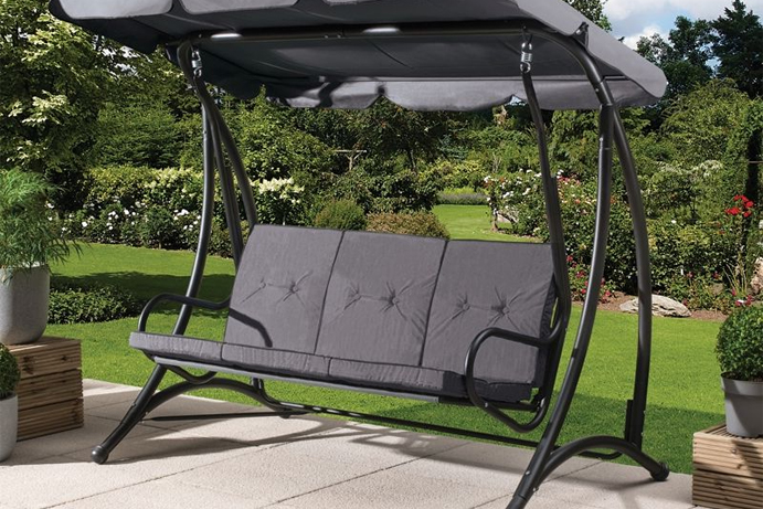 Charcoal grey outdoor swing set on a patio with a garden in the background.