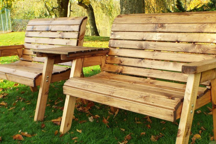 Twin wooden garden benches on grass under an autumn tree.
