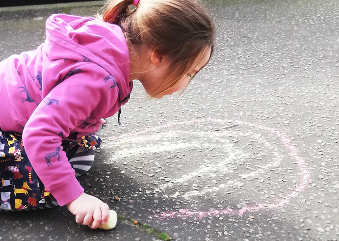 young girl crouching and drawing on a pavement with chalk