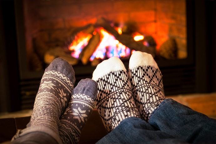 Two pairs of feet in cosy socks resting by an open fire