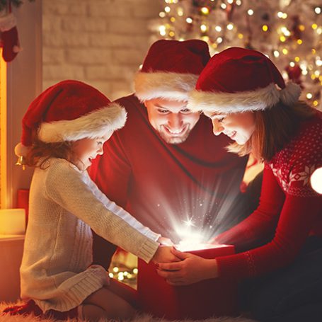 parents and a young girl opening a box under the christmas tree