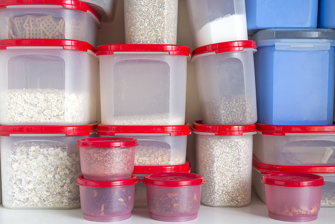 Piled up plastic food storage containers with red lids, filled with a variety of dried foods.