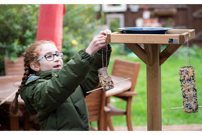 Young girl with glasses hanging a bird feeder on a bird table
