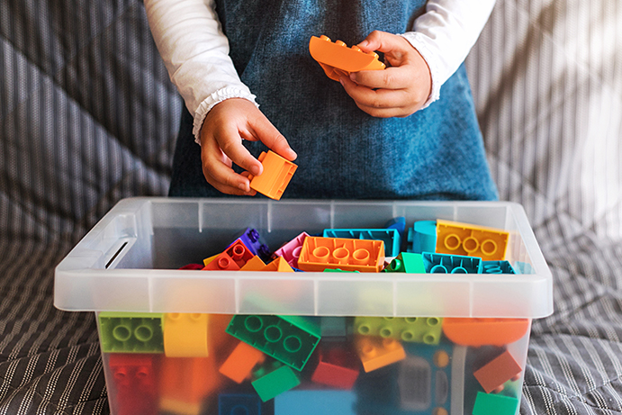 Childs hand sorting plastic blocks into a clear plastic box.