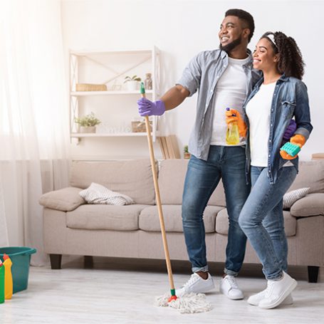 couple standing with cleaning products in a very tidy living room looking accomplished