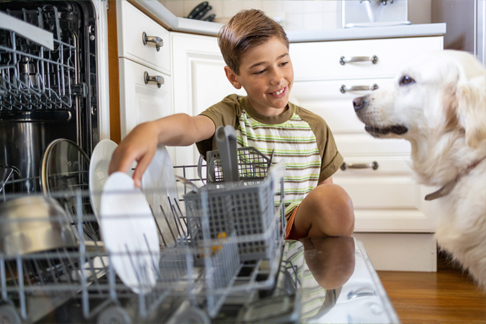 Young boy crouching by a dishwasher and smiling at a golden labrador sitting and watching