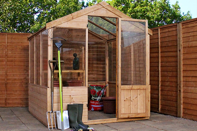 A wooden garden greenhouse with an open door on a patio