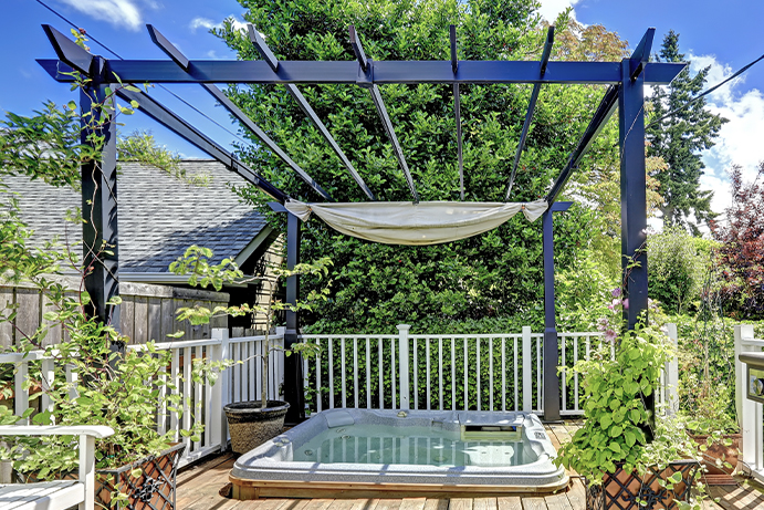 Pergola painted blue standing over a hot tub on decking outdoors