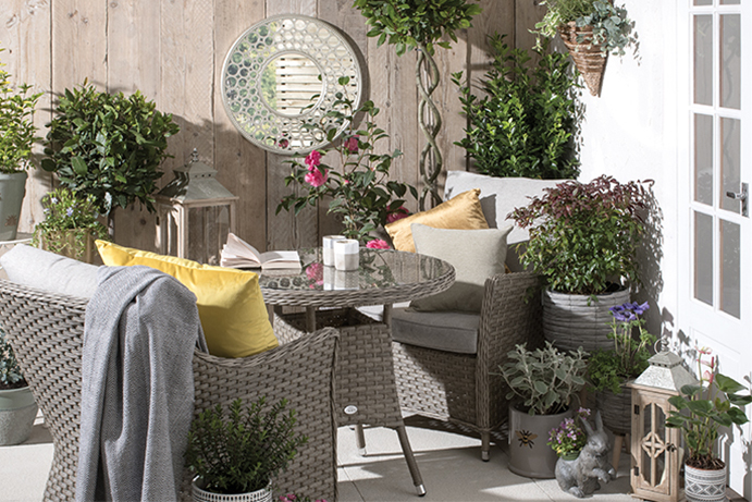 Grey rattan bistro set in a small patio area filled with plants and garden decorations