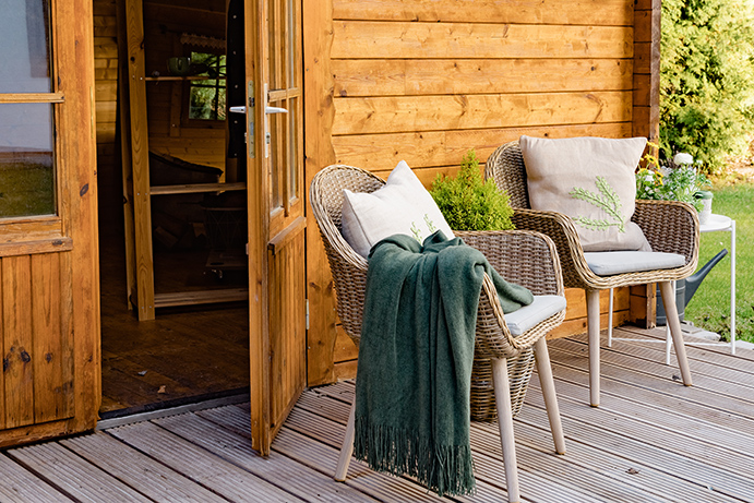 An up close of two rattan armchairs on the porch of a timber garden log cabin