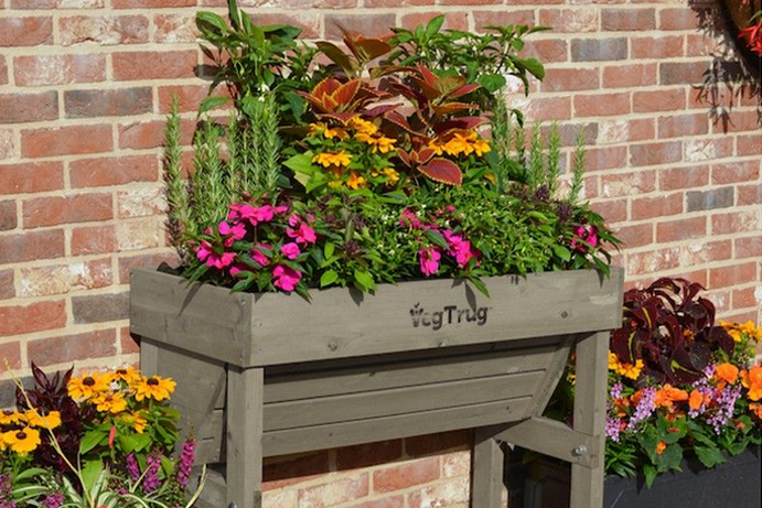 Planter on raised legs against a brick wall and filled with flowers and foliage