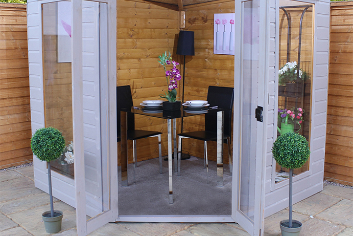 A painted summerhouse with doors wide open and a black and metal dining set inside