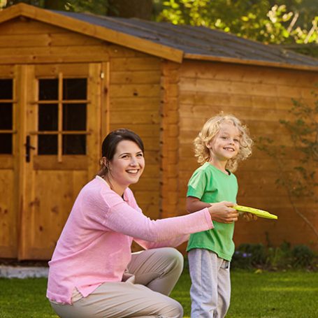 Lady crouching with her young son, both smiling and playing in front of a large garden shed
