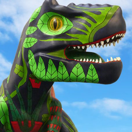 Close up of a painted t-rex head sculpture with a blue sky full of clouds in the background