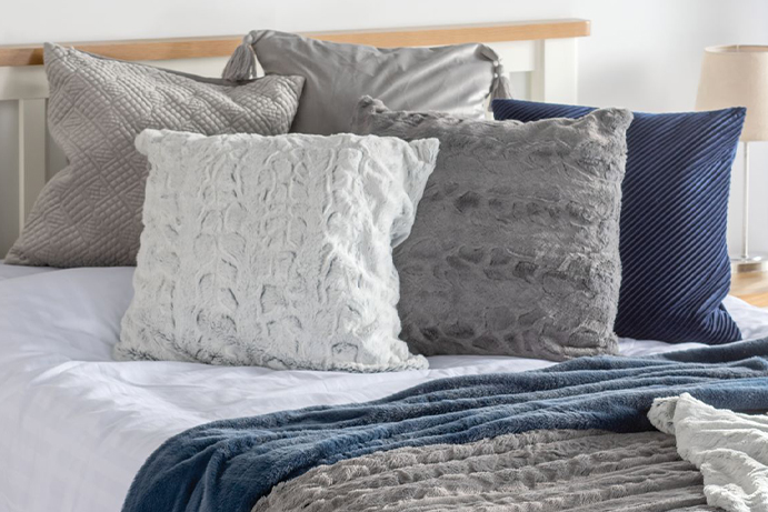 Grey and blue fluffy and velvety cushions scattered on a white double bed