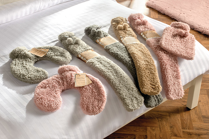 A collection of fluffy hot water bottles laying on the end of a white double bed