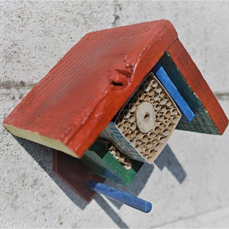 homemade colourful bee hotel hanging on a white wall