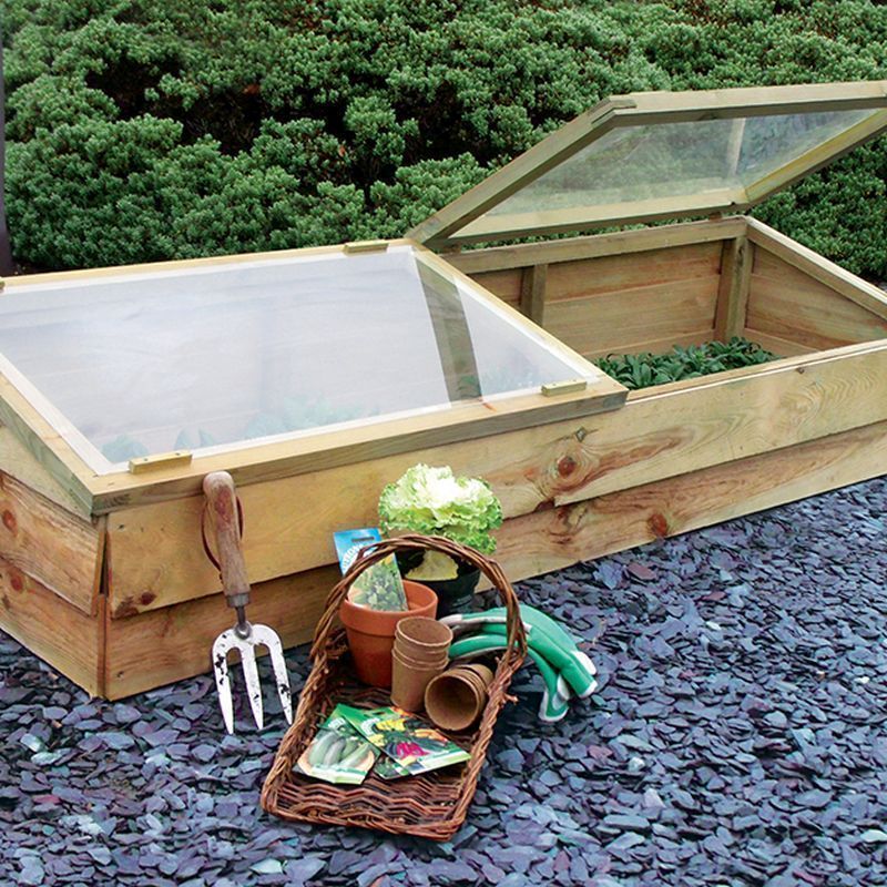 a cold frame with plants inside and gardening tools in a basket